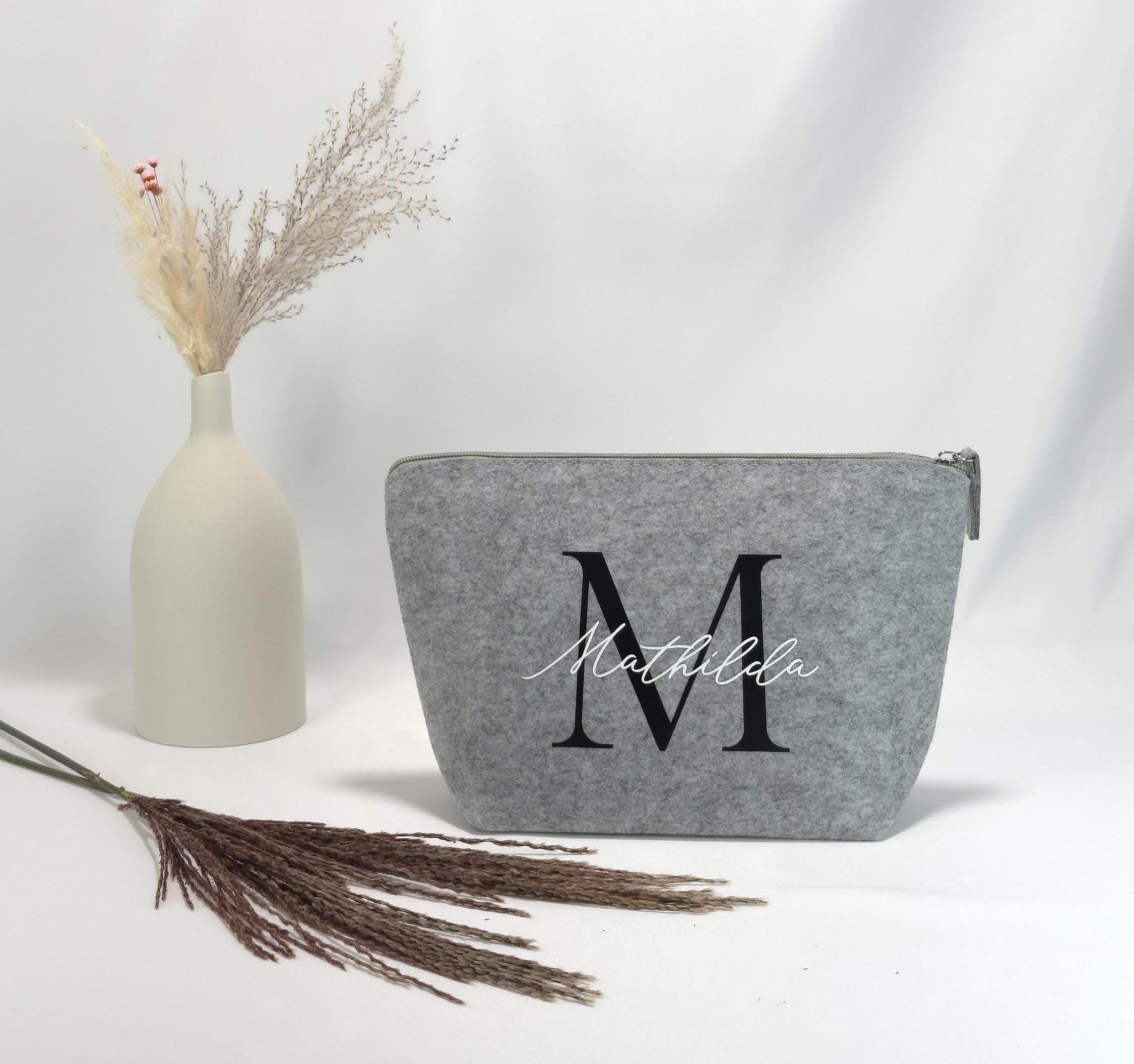Schminktasche personalisiert mit Namen, hochwertige Struktur und goldfarbenem Reißverschluss, geeignet als individuelles Geschenk für Frauen, Tochter oder beste Freundin, fotografiert neben Make-up-Pinseln und Lippenstift.