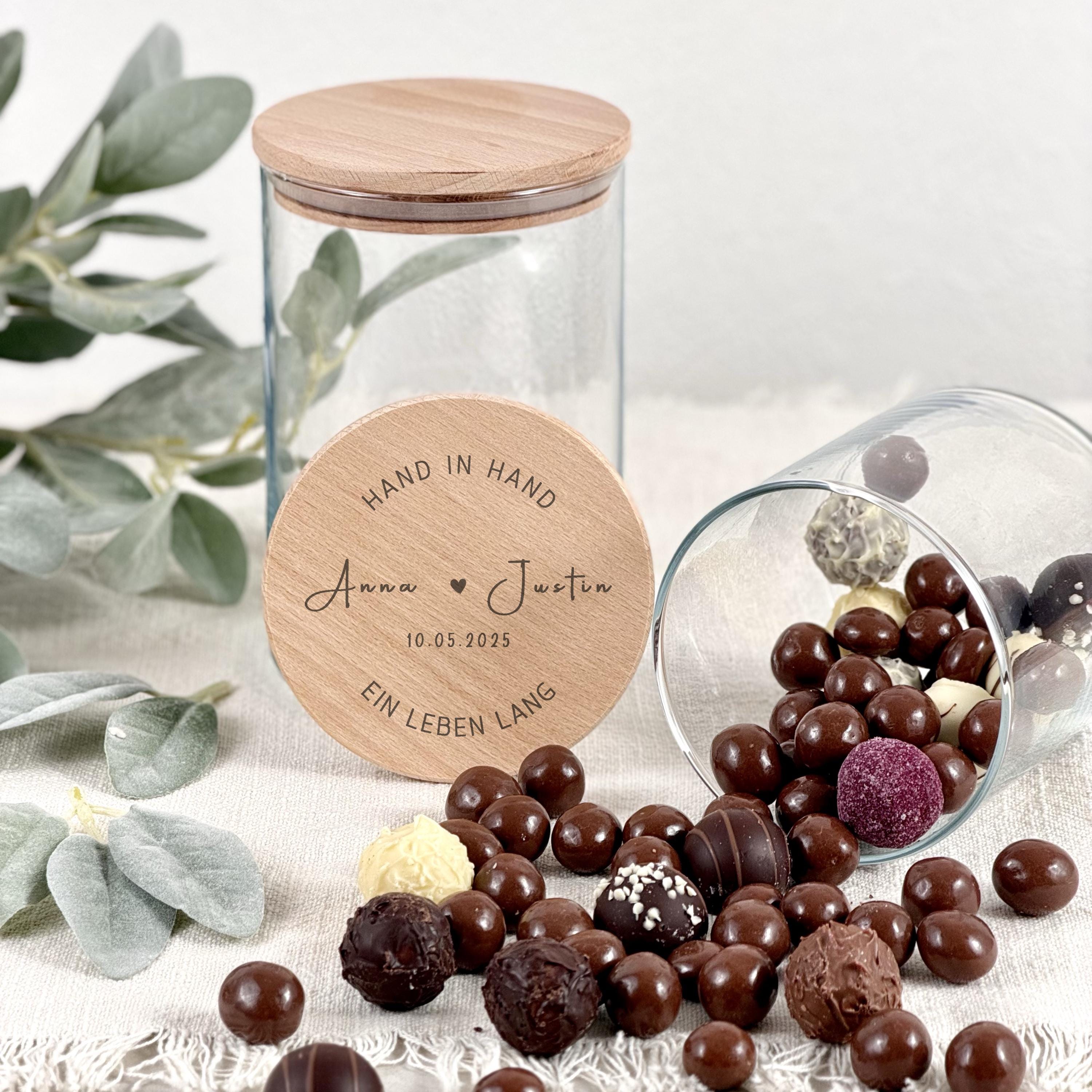 Ein modernes Vorratsglas mit individueller Gravur, das als personalisiertes Geschenk für Paare präsentiert wird. Namen, Herzsymbole und ein schönes Motiv heben die romantische Bedeutung hervor. Das Bild zeigt das Glas auf einer natürlichen Holzoberfläche, umgeben von zarten Deko-Elementen. Das Produkt eignet sich perfekt für Valentinstag, Hochzeit, Verlobung oder als Geldgeschenk. Das Foto unterstreicht die Liebe zum Detail und die hohe Qualität der Gravur.