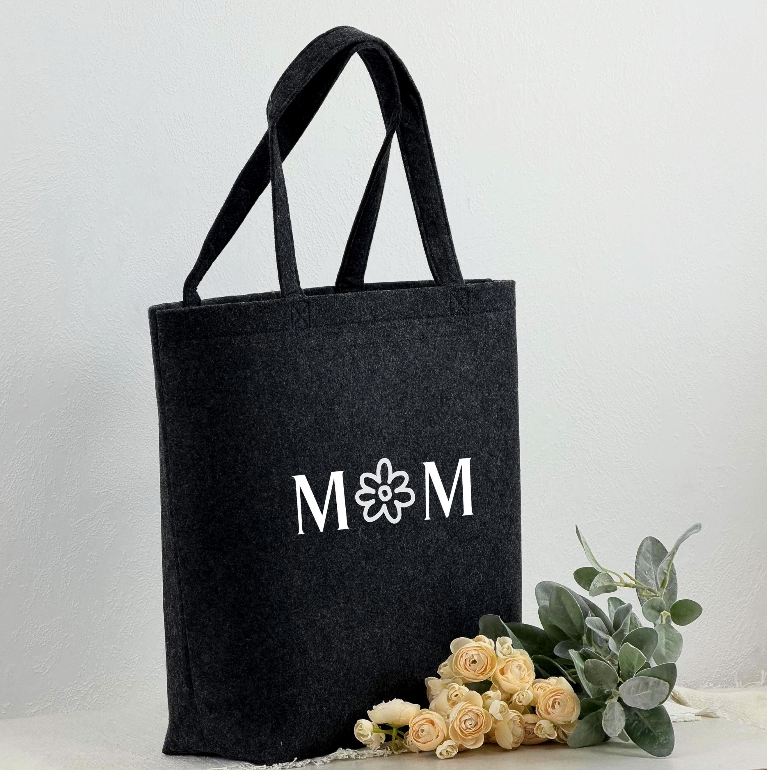 Filztasche für Frauen, personalisiert mit Namen oder individuellem Text, ideal als Geschenk für Mama. Das Bild zeigt die Tasche in einem warmen Licht, umgeben von Deko-Elementen wie Rosen und Geschenkpapier. Perfekt als Muttertagsgeschenk, Weihnachtsgeschenk oder Geburtstagsgeschenk. Die Tasche ist sowohl praktisch als Shopper als auch als dekoratives Accessoire nutzbar.