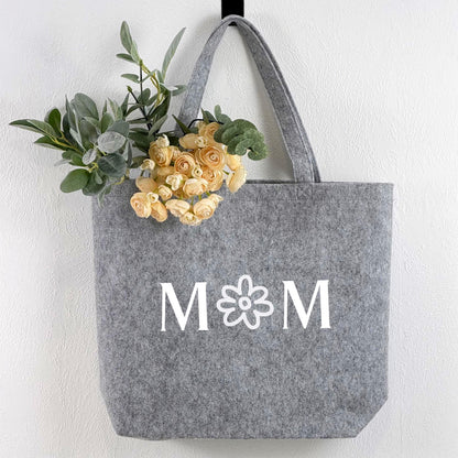 Eine personalisierte Filztasche als einzigartiges Geschenk für Mütter. Die Tasche zeigt den eingestickten Namen oder Wunschtext des Beschenkten und wird auf einem hellen Hintergrund mit Dekorationen fotografiert. Perfekt geeignet als Geburtstagsgeschenk, Muttertagsgeschenk oder Weihnachtsgeschenk. Hochwertiges Filzmaterial sorgt für Langlebigkeit und Stil.