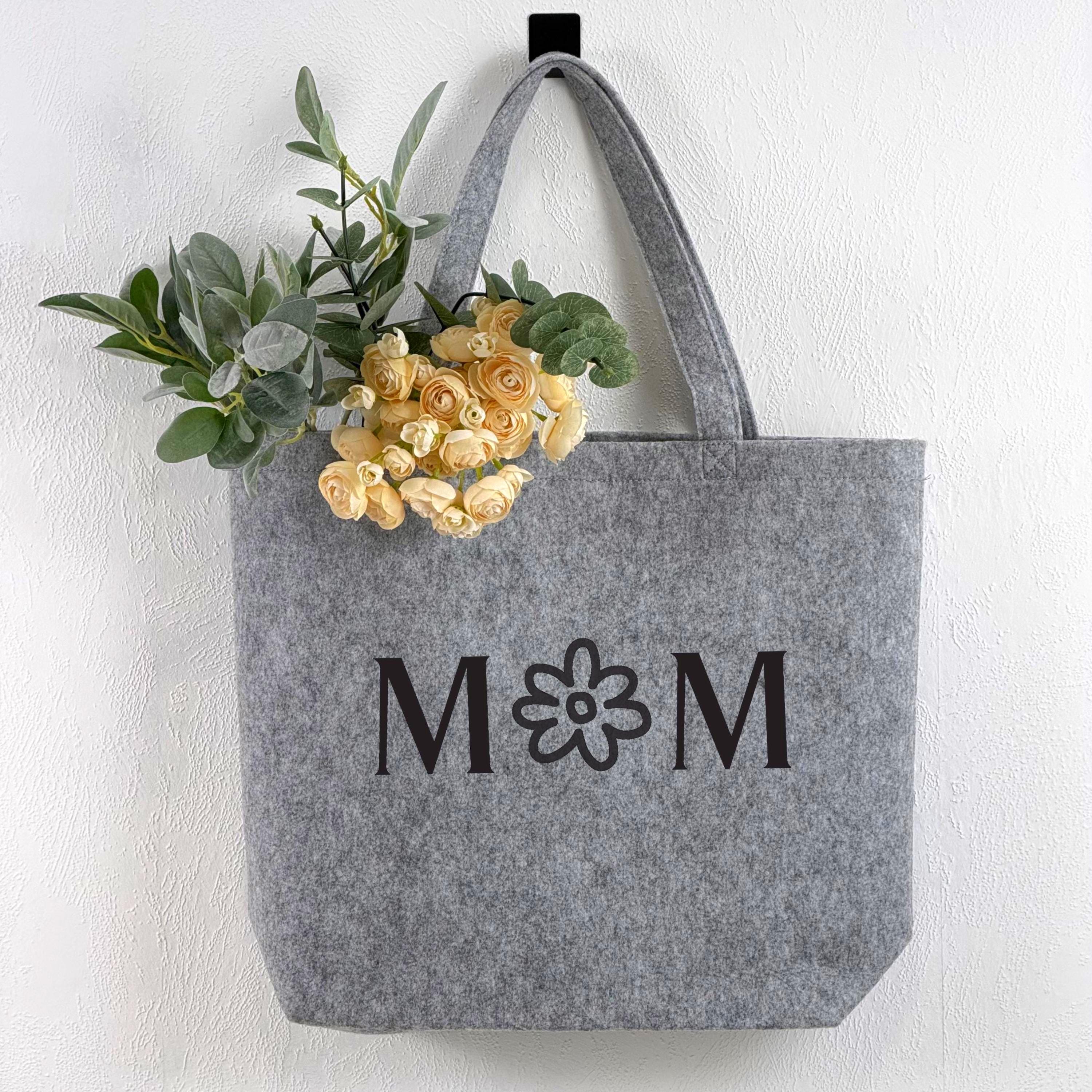 Hochwertige, personalisierte Shoppertasche aus Filz für Mama. Mit eingesticktem Namen oder Text, stilvoll, robust und praktisch. Das Bild zeigt die Tasche in einer warmen, freundlichen Umgebung mit Dekorationen, die Liebe, Wertschätzung und Alltagstauglichkeit kombinieren. Ideal als Geschenkidee für Mütter, Geburtstage, Weihnachten oder Muttertag.