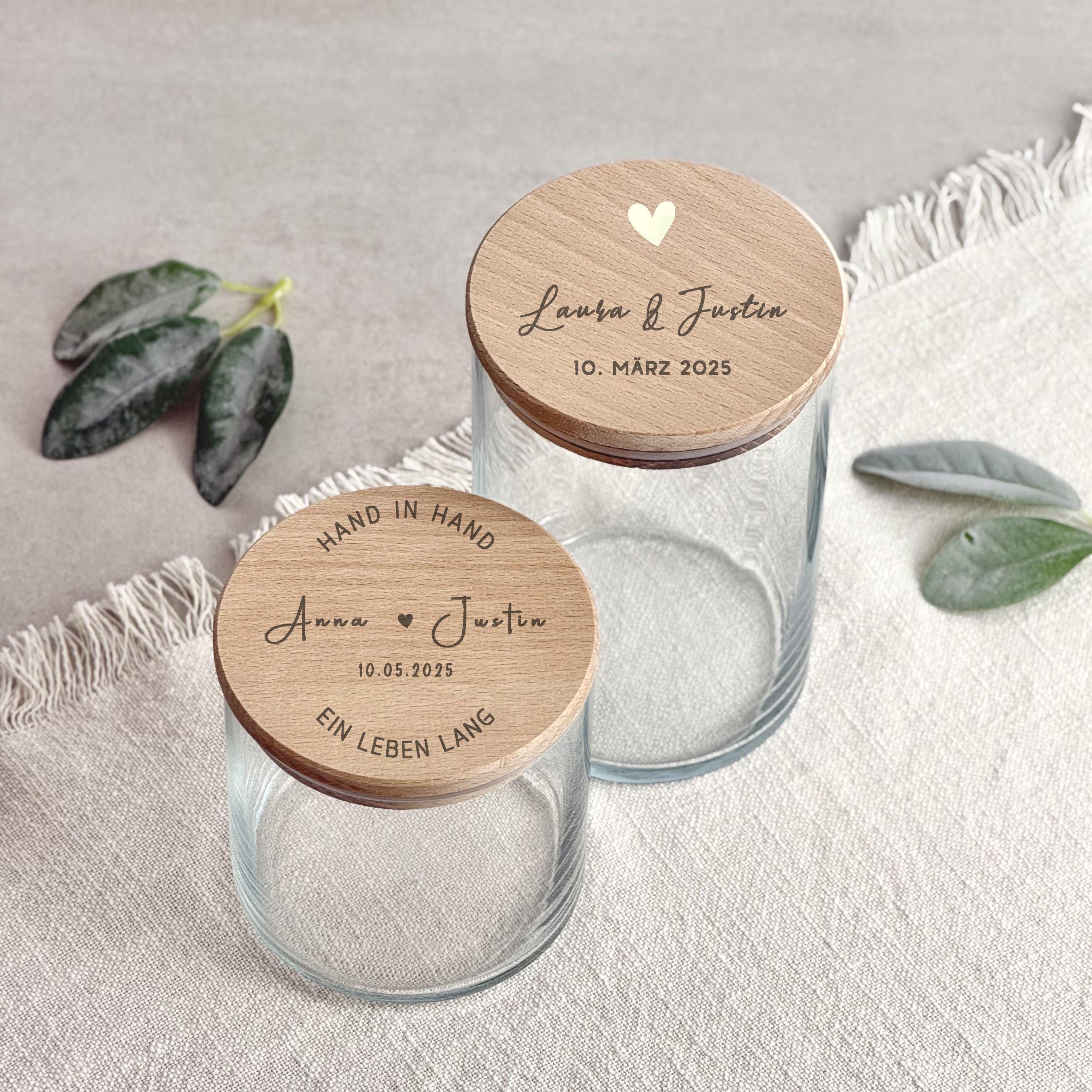 Ein personalisiertes Vorratsglas mit eleganter Gravur für Paare. Das Glas zeigt zwei eingravierte Namen sowie ein dekoratives Motiv, ideal als romantisches Paargeschenk. Das Glas steht auf einem Holztisch im warmen Licht, umgeben von kleinen Deko-Elementen wie Herzen oder Blumen. Perfekt als Valentinstag Geschenk, Hochzeitsgeschenk oder Brautpaar Geschenk. Das hochwertige Glas dient als stilvolle Aufbewahrung und zugleich als emotionales Erinnerungsstück für besondere Momente.