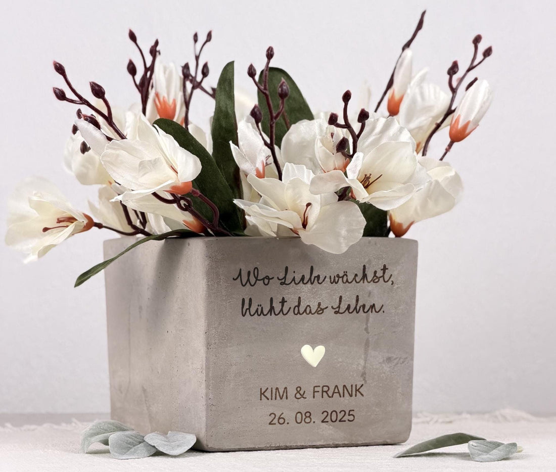Ein Blumentopf mit personalisierter Gravur, perfekt als Geschenk für Brautpaare. Die matte Oberfläche des Topfes und die sanfte Lasergravur erzeugen ein hochwertiges, elegantes Erscheinungsbild. Im Inneren befindet sich eine kleine Pflanze, die dem Geschenk Leben und Frische verleiht. Ideal als Hochzeitsgeschenk mit Name, kreative Geldgeschenk-Idee oder Deko im neuen Zuhause bei Einzug oder Einweihung.