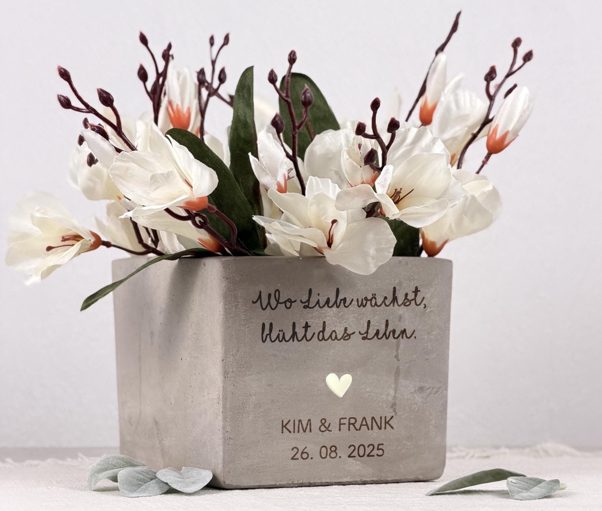 Ein Blumentopf mit personalisierter Gravur, perfekt als Geschenk für Brautpaare. Die matte Oberfläche des Topfes und die sanfte Lasergravur erzeugen ein hochwertiges, elegantes Erscheinungsbild. Im Inneren befindet sich eine kleine Pflanze, die dem Geschenk Leben und Frische verleiht. Ideal als Hochzeitsgeschenk mit Name, kreative Geldgeschenk-Idee oder Deko im neuen Zuhause bei Einzug oder Einweihung.