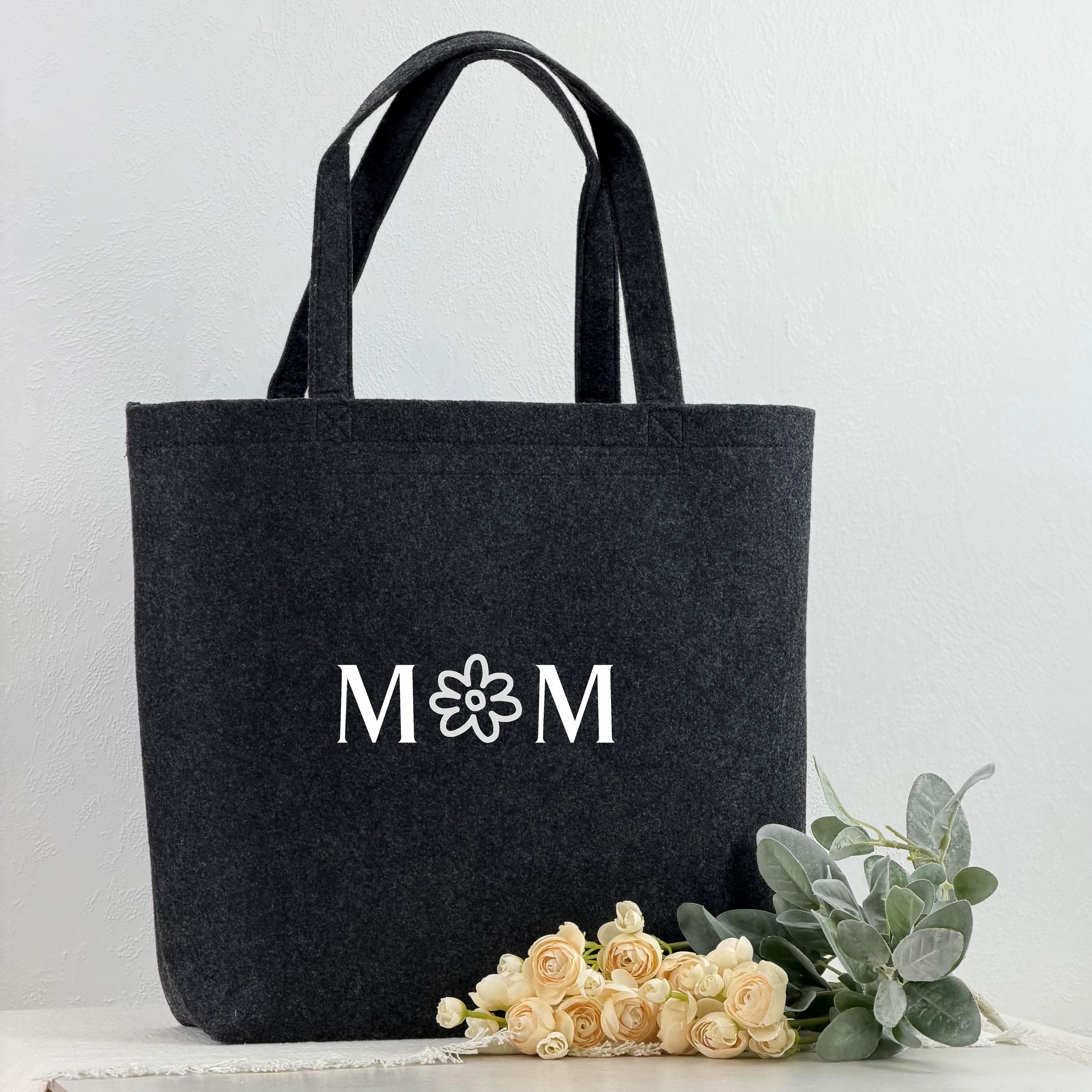 Hochwertige personalisierte Filztasche für Frauen, ideal als Mama Geschenk. Mit eingesticktem Namen wird diese Tasche zu einem einzigartigen Andenken, das praktischen Nutzen und emotionale Bedeutung kombiniert. Das Foto zeigt die Tasche in Nahaufnahme, auf einem Tisch dekoriert mit Herz- und Blumenmotiven, perfekt für Valentinstag, Muttertag oder Geburtstagsgeschenke.