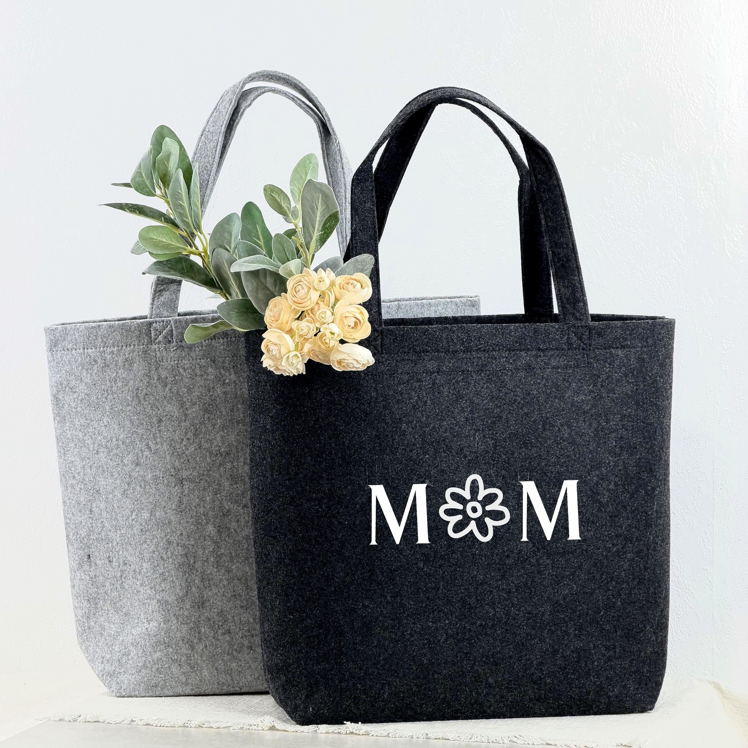 Ein personalisiertes Mama Geschenk: eine hochwertige Filztasche mit individuell eingesticktem Namen oder Wunschtext. Die Tasche ist stilvoll, robust und vielseitig einsetzbar für Alltag, Shopping oder Freizeit. Perfekt als Geburtstagsgeschenk, Muttertagsgeschenk oder Weihnachtsgeschenk. Das Foto zeigt die Tasche auf einem hellen Hintergrund mit dekorativen Elementen, die Wärme, Liebe und Praktikabilität vermitteln.