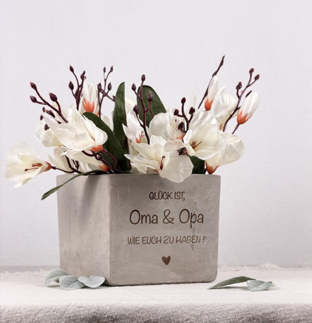 Ein personalisierter Blumentopf mit dem liebevollen Spruch „Glück ist Oma und Opa wie euch zu haben“, perfekt als Geschenk für Großeltern zu Geburtstag, Weihnachten oder Muttertag. Der individuelle Blumentopf eignet sich ideal für Pflanzen und Blumen und wird mit Namen oder Wunschtext personalisiert. Dieses dekorative Geschenk ist eine herzliche Aufmerksamkeit für Oma, Opa, Eltern oder Familie und bringt Wärme, Liebe und Wertschätzung in jedes Zuhause.