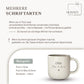 May include: Two ceramic mugs, one black with white speckles and the word "SCHWARZ", the other white with speckles and the word "WEIB". Both mugs have a tan-coloured base and a curved handle. The mugs are stacked on top of each other.