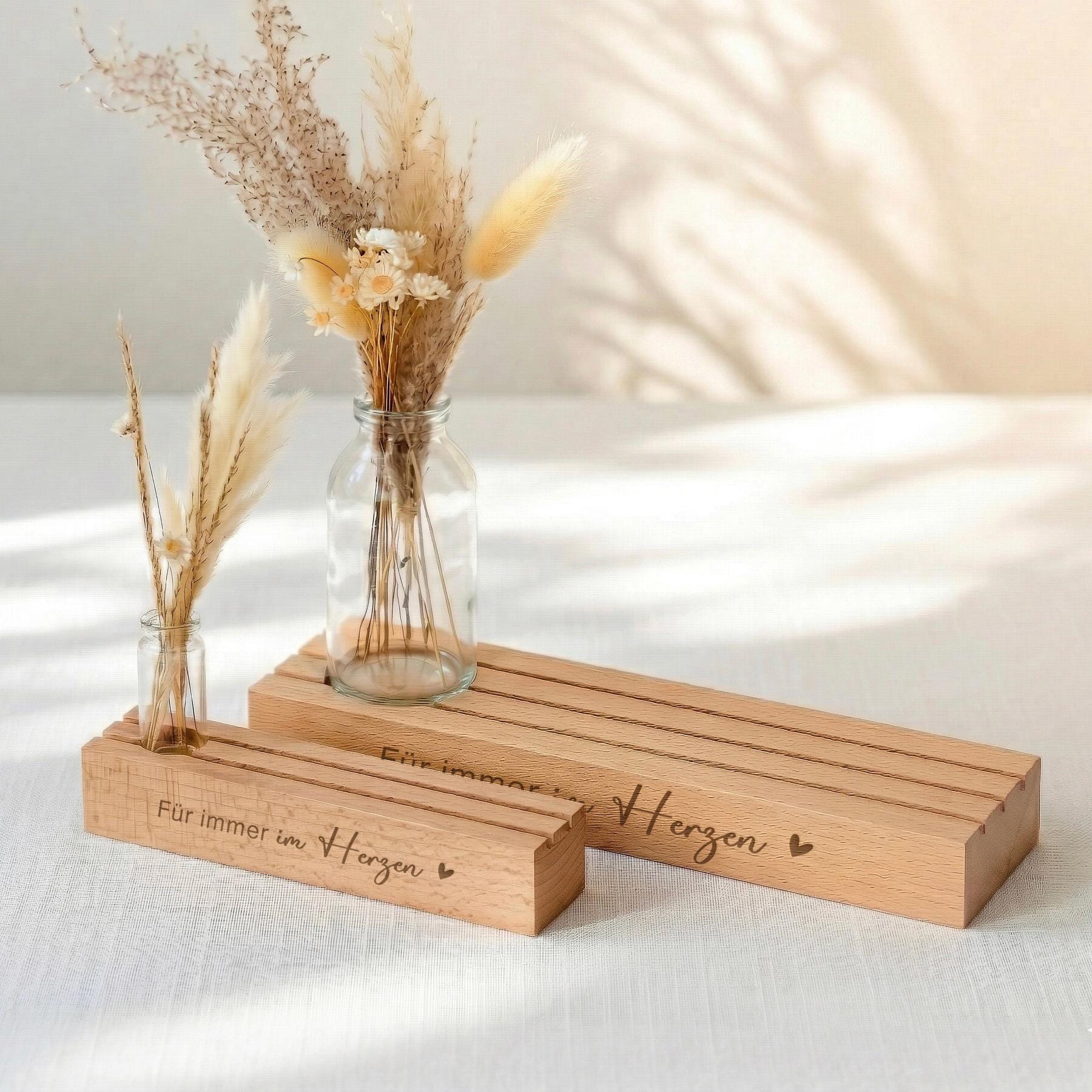 Kartenständer mit Gravur „Für immer im Herzen“ als Kartenhalter personalisiert mit Vase und Trockenblumen. Diese Bilderleiste aus Buchenholz ist ein würdevolles Trauergeschenk individuell gestaltet. Der Fotoständer personalisiert eignet sich zum Aufstellen von Erinnerungsfotos oder Beileidskarten. Integrierter Kerzenhalter für Gedenkkerze ergänzt das Geschenkset Beileid Erinnerung und macht dieses Kondolenzgeschenk zu einer liebevollen Aufmerksamkeit bei Trauerfall oder Beerdigung.