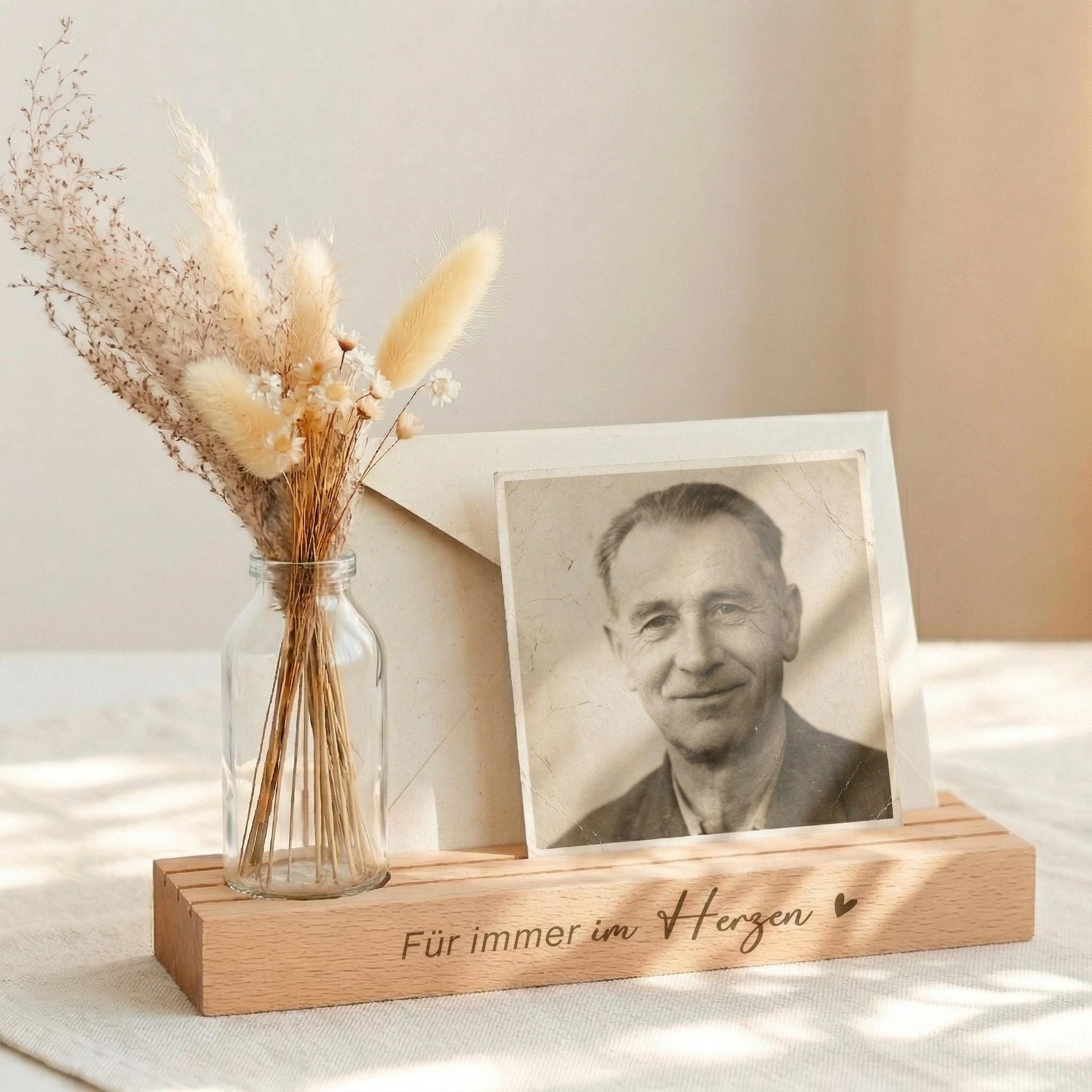Kartenständer mit Gravur „Für immer im Herzen“ als Kartenhalter personalisiert mit Vase und Trockenblumen. Diese Bilderleiste Bilderrahmen aus Buchenholz ist ein einfühlsames Trauergeschenk individuell gestaltet. Ideal als Kondolenzgeschenk Beileid oder Geschenk Anteilnahme. Der Fotoständer personalisiert kombiniert Kerzenhalter für Gedenkkerze mit dekorativer Vase und eignet sich als Geschenk Beerdigung oder Erinnerung.
