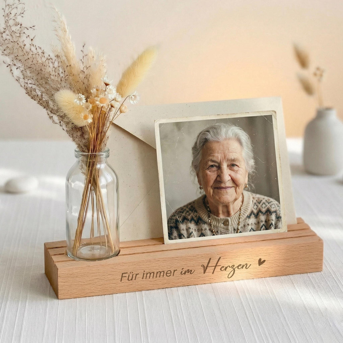 Kartenhalter personalisiert mit Vase und Trockenblumen als Trauergeschenk individuell aus Buchenholz gestaltet. Die Bilderleiste mit Gravur „Für immer im Herzen“ bietet Platz für Fotos, Kondolenzkarten und Erinnerungen. Der Kartenständer mit Gravur eignet sich als Kondolenzgeschenk Beileid oder Geschenk Anteilnahme. Fotoständer personalisiert kombiniert Kerzenhalter für Gedenkkerze und Vase zu einer stilvollen Gedenkseite als Geschenk Beerdigung oder Beileid Geschenk Trauer.
